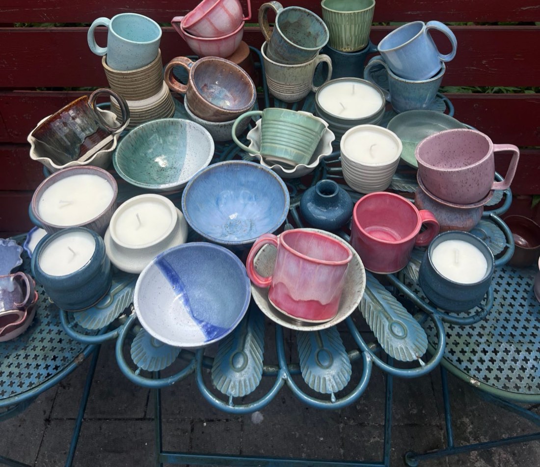 A table crowded with Spindle Lane's handmade mugs, bowls, and candles in soft pinks, blues, and greens